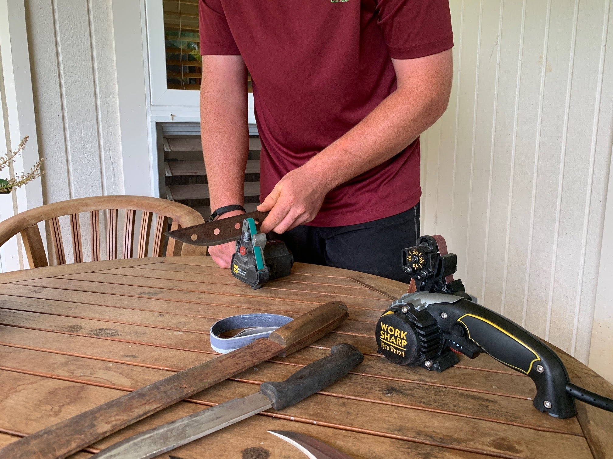 A man uses a Ken Onion Edition Sharpener to sharpen a large fixed blade on top of a table front view